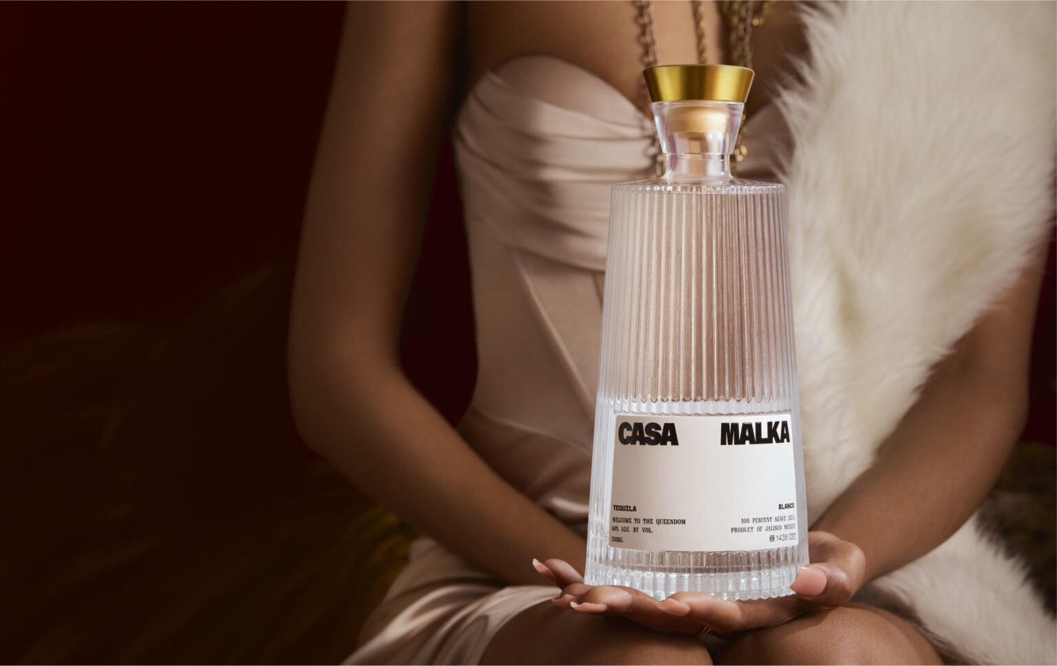 Woman in a fur dress holding Casa Malka Blanco Tequila bottle, showcasing luxury and elegance