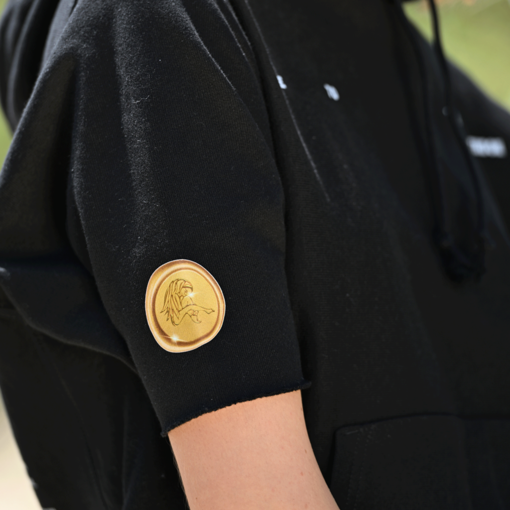 Close-up of gold emblem on the sleeve of Casa Malka black hoodie